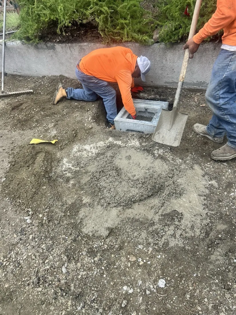 Crew setting a concrete catch basin drainage box at a graded site